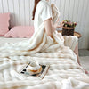 A person is wrapped in a fluffy cream colored rabbit fur throw blanket indoors.