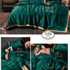A luxurious emerald green ice silk blanket set featuring gold embroidery and a matching satin pillow in a bedroom setting.