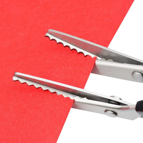 A pair of professional stainless steel pinking shears resting on a red piece of paper.