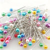 A cluster of decorative sewing and pinning needles in various colors including blue, green, pink, purple, and gold.