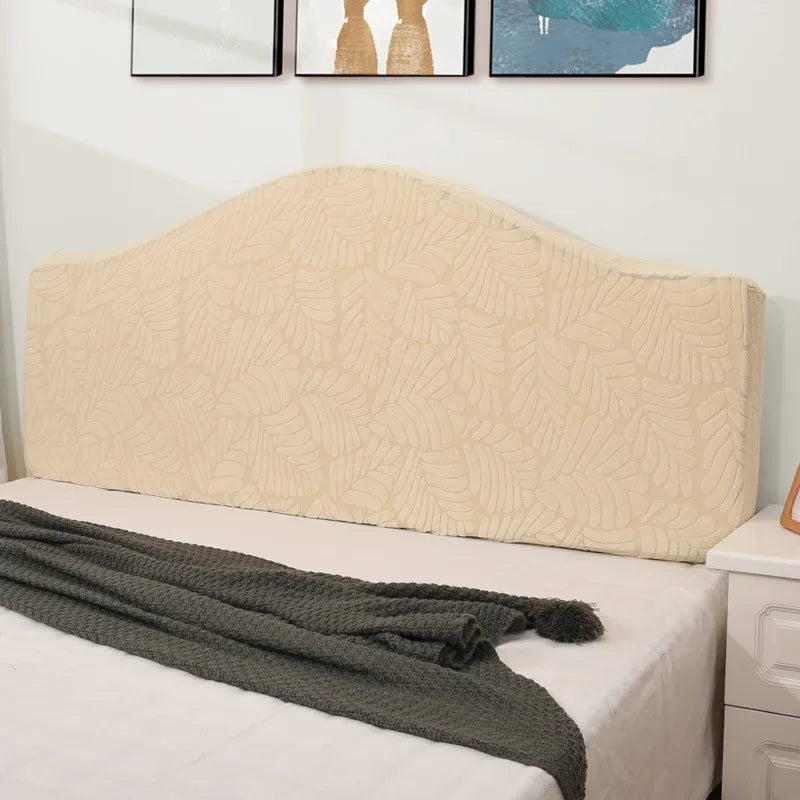 A beige soft elastic headboard cover on a white bed with a dark gray throw blanket.