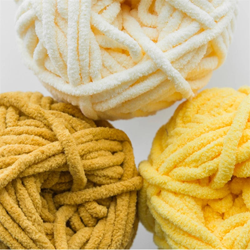 A close-up of three balls of thick velvet yarn in shades of cream, yellow, and gold.