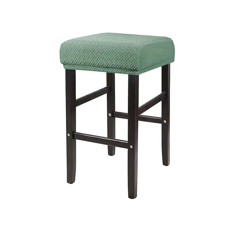 A green fabric bar stool slipcover with dark wooden legs and a textured seat.