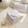 A stack of white and lavender quilted pillows with a floral pattern on a light-colored surface.