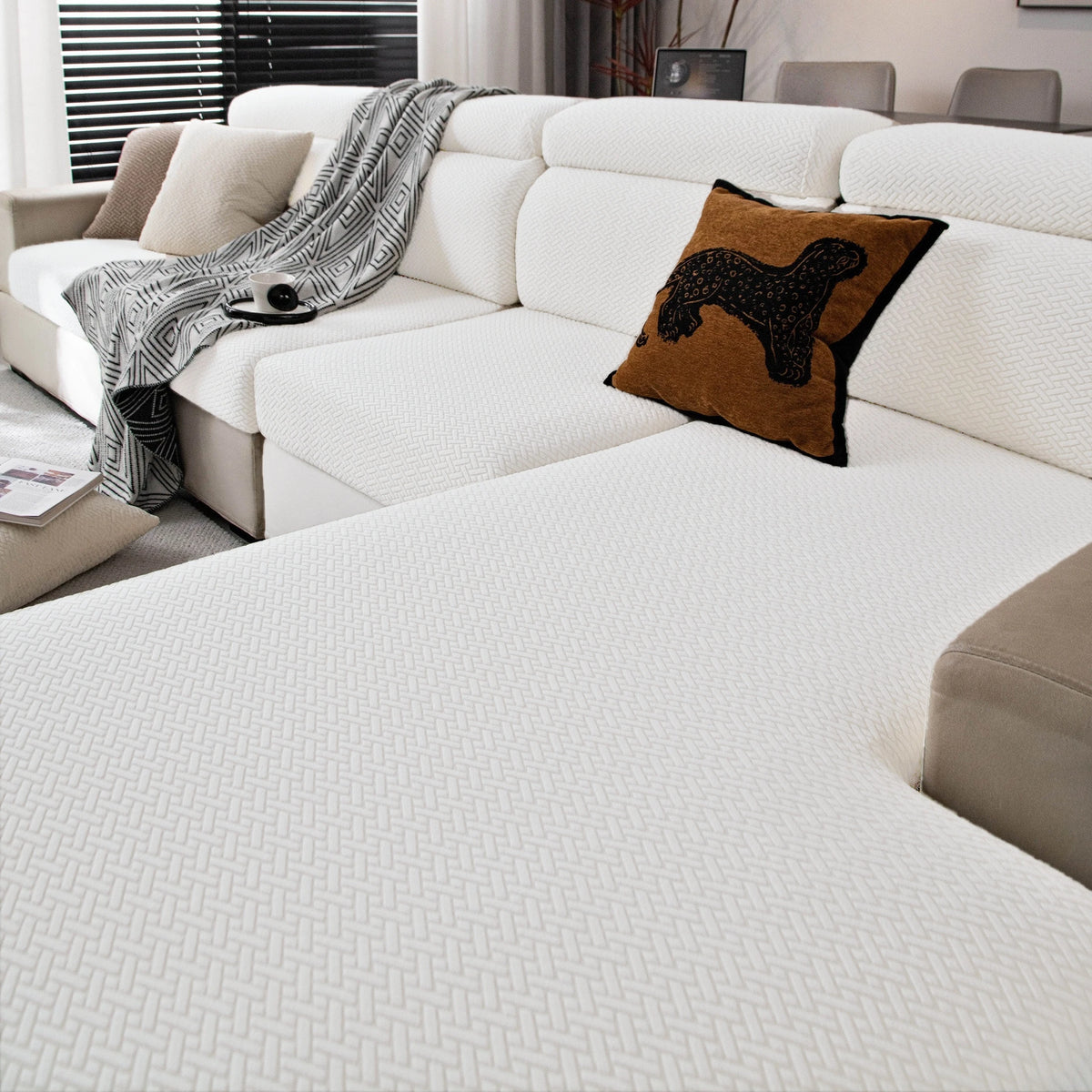 A white stretchy polar fleece sofa cover with a patterned throw and an accent pillow on a modern sofa.