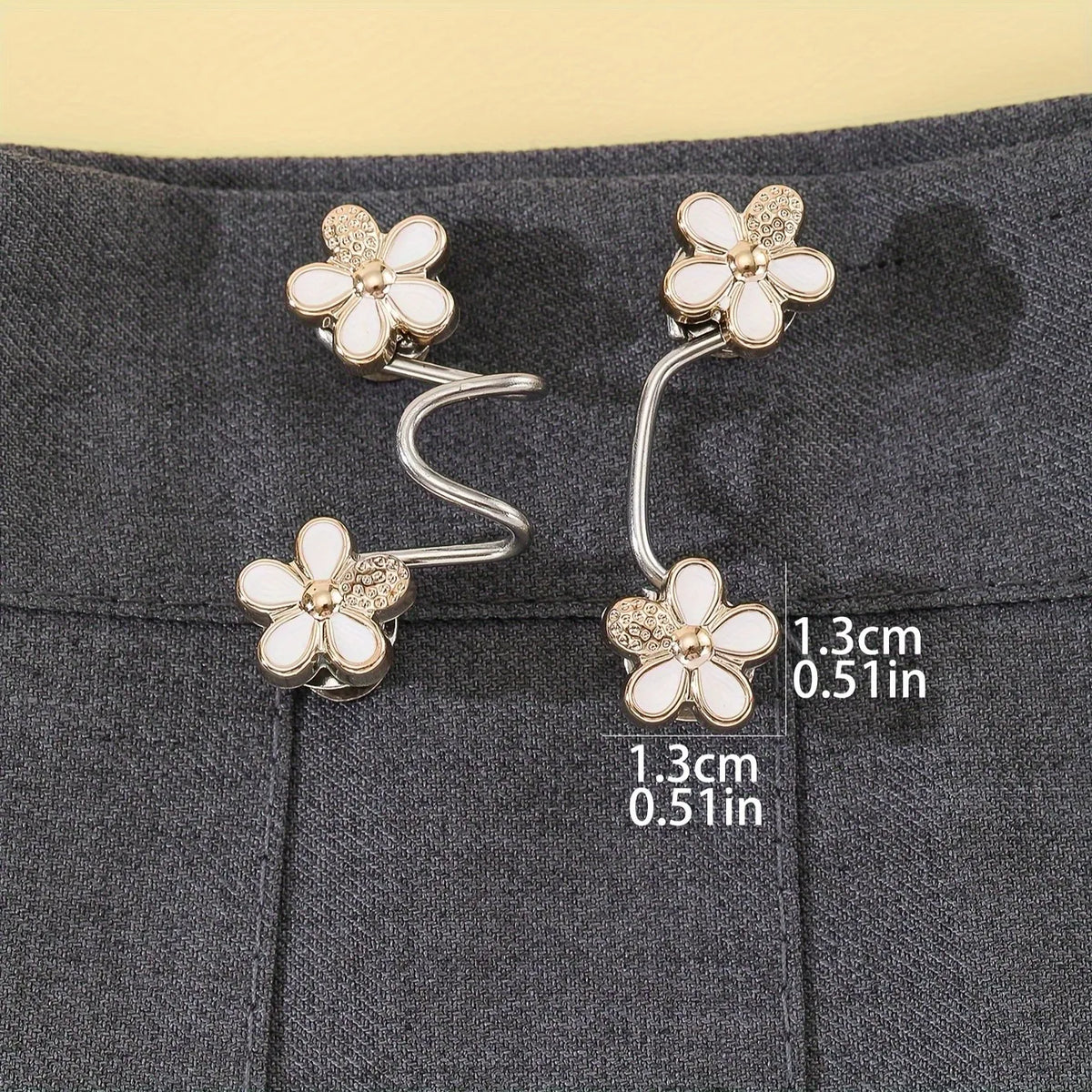 Gold and white floral adjustable buckles used as waist tighteners on gray fabric.