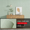 Self-adhesive 3D thermal insulation wallpaper in linen texture on a wall with wooden furniture and green fabric.