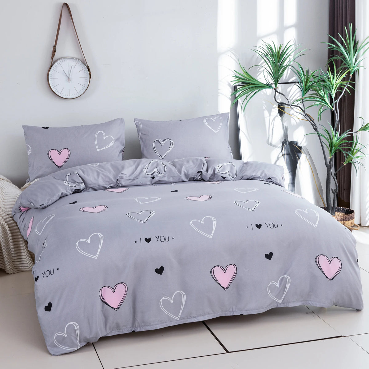 A gray bedding set featuring a pink heart print duvet cover and pillowcases on a bed.
