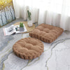 A brown tufted corduroy floor seat cushion resting on a light gray patterned rug near a window.