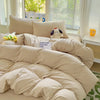 A beige solid cotton bed linen set with pillows and a duvet on a bed near a window.