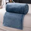 A folded teal flannel throw blanket resting on a white sofa.