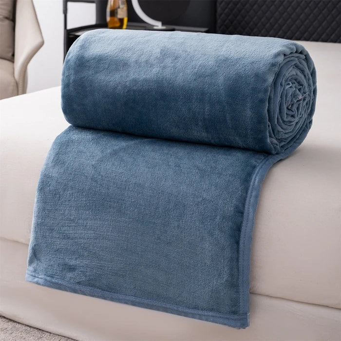 A folded teal flannel throw blanket resting on a white sofa.