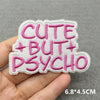 Pink embroidered patch with the text CUTE BUT PSYCHO on a gray fabric background