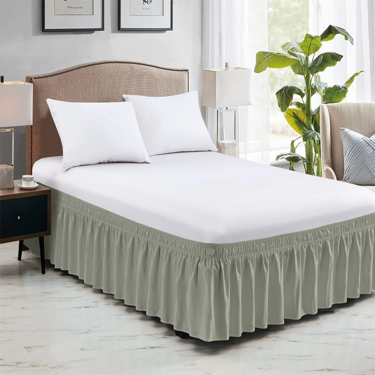 A white bed with a long, pleated sage green elastic bed skirt and white pillows in a bedroom setting.