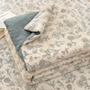 A stack of light beige and gray cartoon quilting comforters with a floral pattern are displayed on a bed.