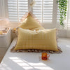 A yellow and white gingham plaid pillow with a ruffled edge resting on a white surface near a window.
