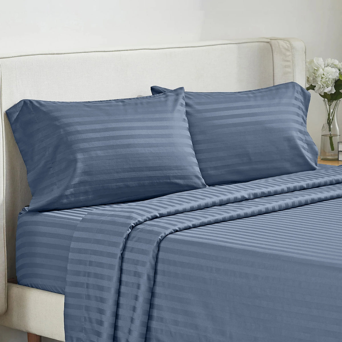 A navy blue striped bedding set featuring a duvet cover, sheet, and pillow on a white upholstered bed.