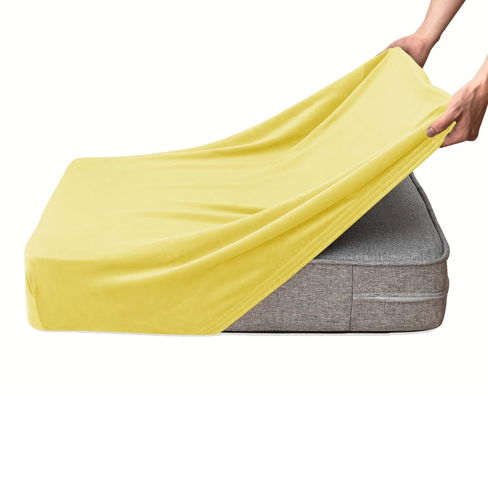 A hand is draping a bright yellow velvet stretchy sofa seat cover over a gray cushion.