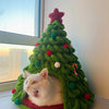 A white cat peeking out of a hand-woven green Christmas tree made from chunky chenille yarn.
