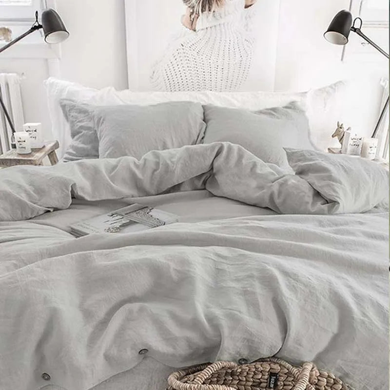 A close-up of a light gray luxury French linen duvet cover on a bed with white pillows and bedside lamps.