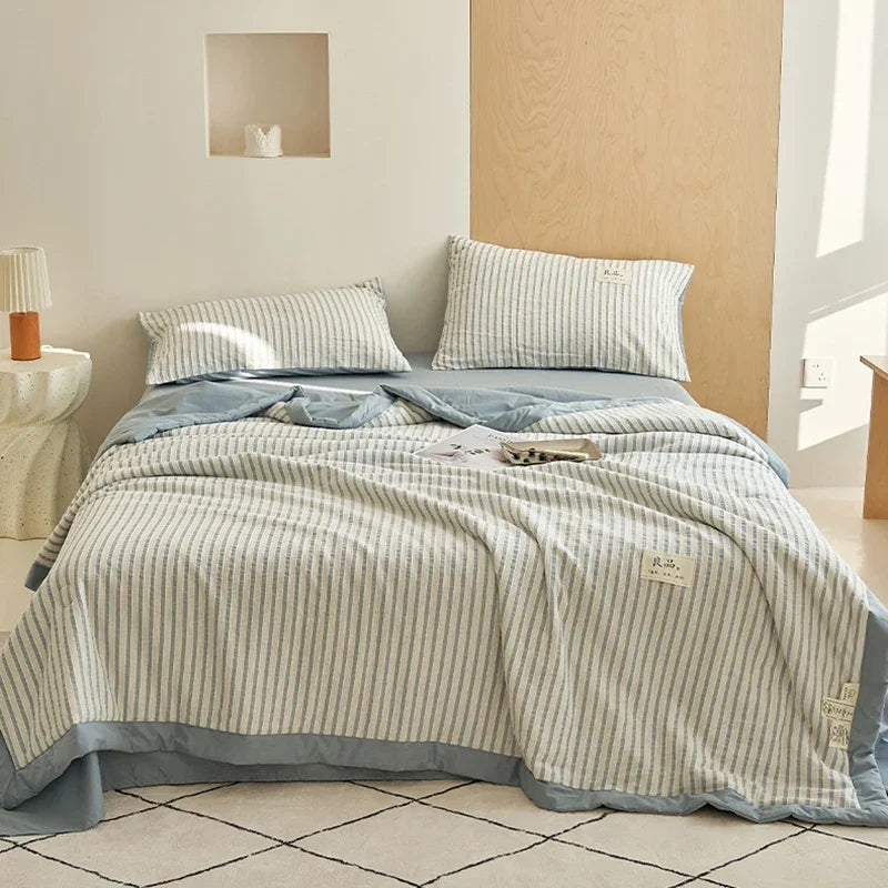 A light blue and white striped luxury jacquard summer quilt is displayed on a bed with neutral bedding.