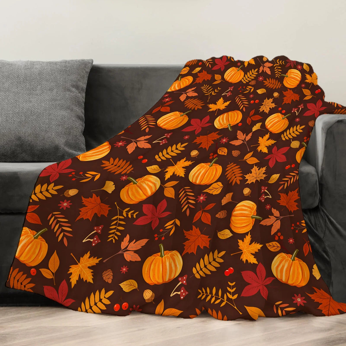 A dark orange and brown autumn leaf patterned fleece throw blanket draped over a gray sofa.