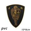 A black shield patch with gold embroidery featuring an angel and a cross, labeled PVC.