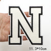 A hand holds a white letter N patch with black outline and embroidery on a white background.