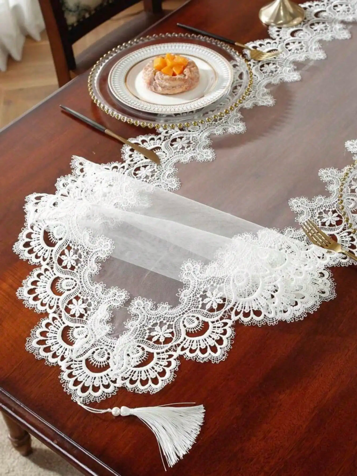 A dark wooden table is decorated with an embroidered mesh lace table runner and gold cutlery.