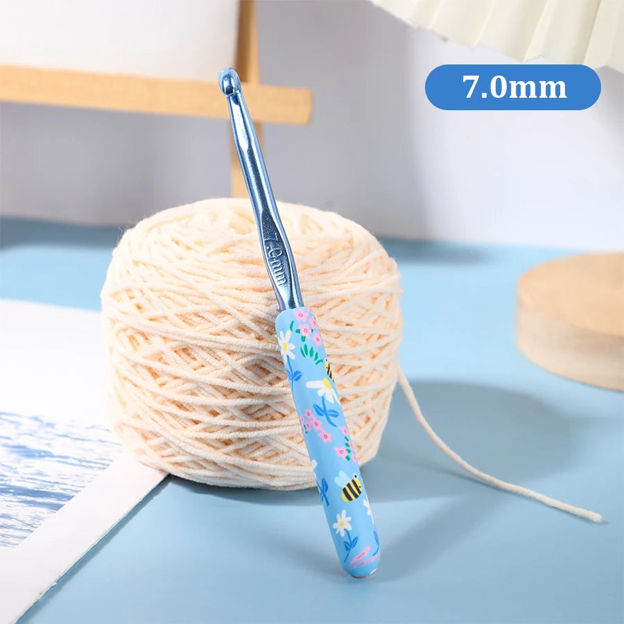A blue ergonomic crochet hook with a floral design is shown next to a ball of light-colored yarn.