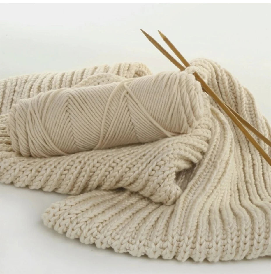 A ball of cream colored yarn is shown next to two wooden knitting needles on a white background.