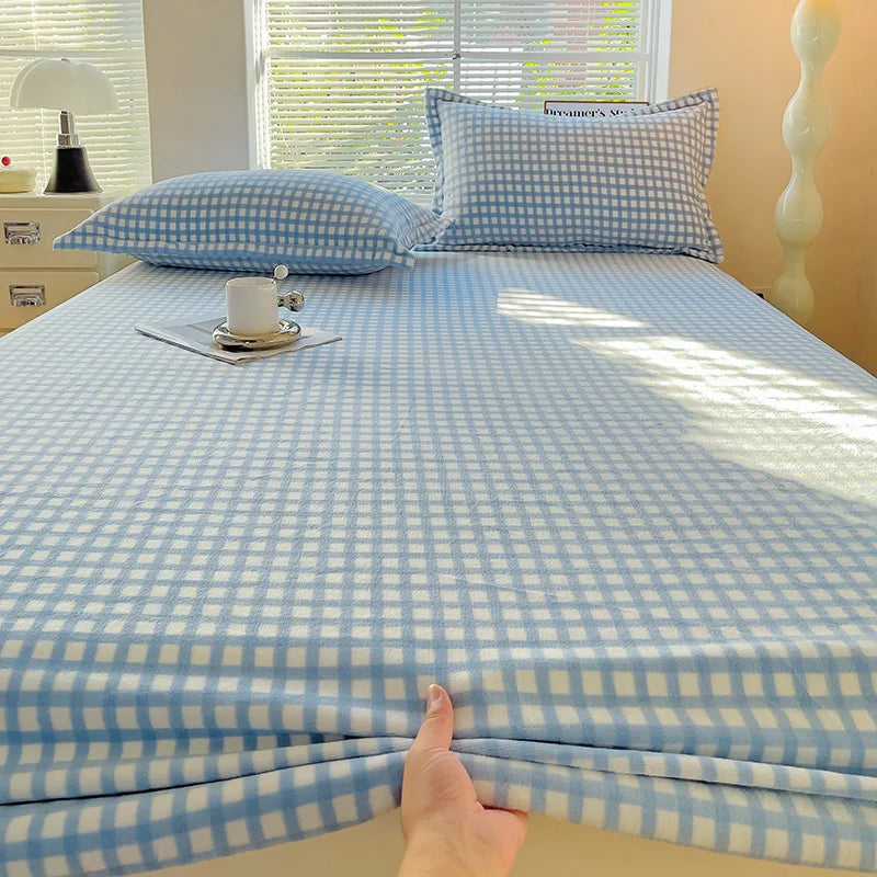 A light blue and white checkered flannel fitted sheet is laid out on a bed with matching pillows.