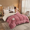 A pink weighted fleece blanket is displayed on a bed, with a woman resting her head on it in a softly lit bedroom.