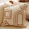 A cream-colored knit pillow cover featuring geometric, arched, and triangular embroidered patterns in tan thread.