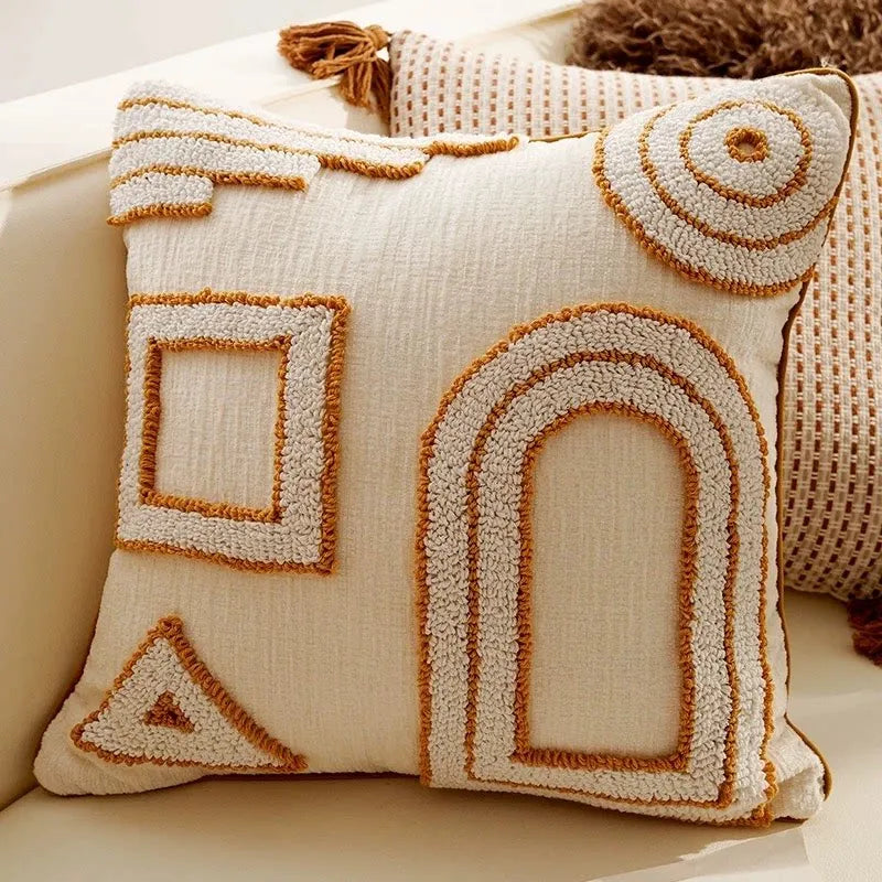 A cream-colored knit pillow cover featuring geometric, arched, and triangular embroidered patterns in tan thread.