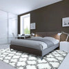 A geometric plush white and black patterned area rug placed in front of a modern gray bed.
