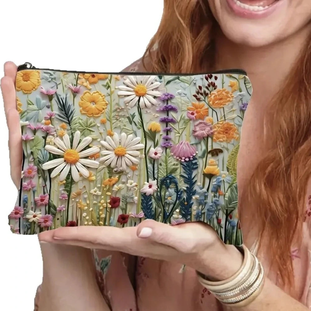 A hand holds a floral double-sided cosmetic storage pouch featuring various dried flowers and greenery.