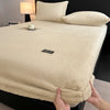 A beige plush jacquard mattress cover is shown on a bed, with pillows and a lamp in the background.