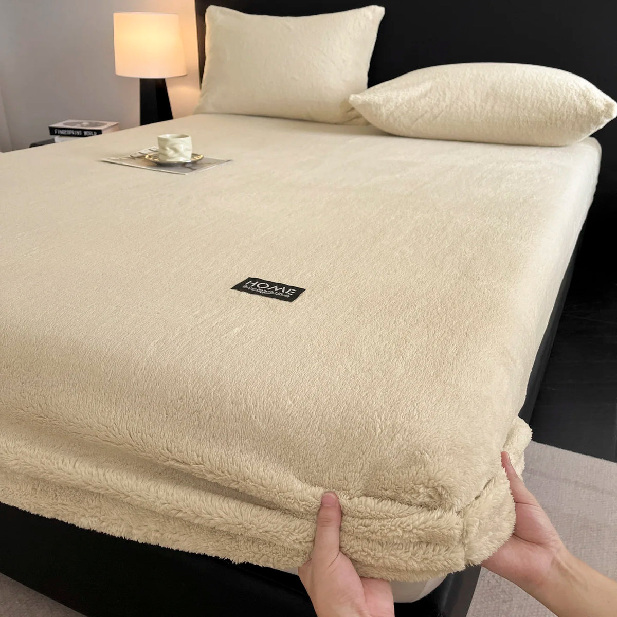 A beige plush jacquard mattress cover is shown on a bed, with pillows and a lamp in the background.