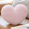 A soft pink heart-shaped plush cushion resting on a beige fabric surface.