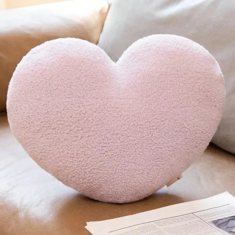 A soft pink heart-shaped plush cushion resting on a beige fabric surface.