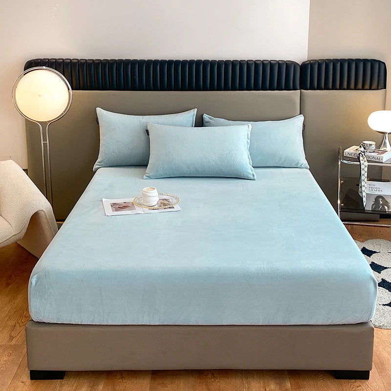 A light blue luxury velvet bedding set displayed on a bed with a dark upholstered headboard.