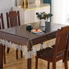 A dark wood dining table set with a lace embroidered PVC tablecloth and wooden chairs.