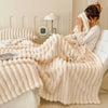 A fluffy cream fleece throw blanket draped over a white bed, next to a lamp and clock.