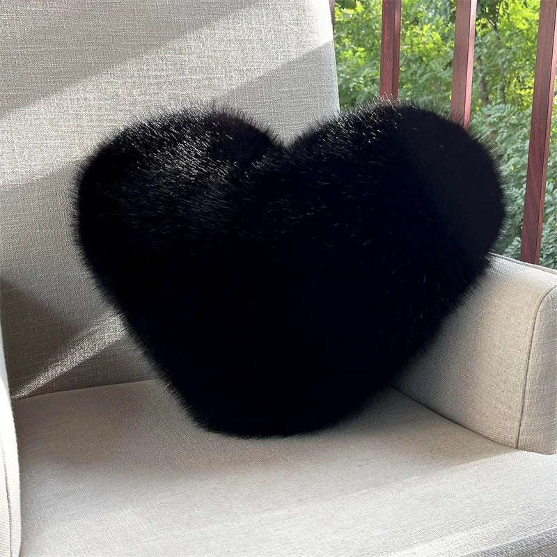A black heart-shaped fox fur throw pillow resting on a light-colored sofa.