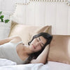 A woman rests her head on a pillow in a bed with a silky satin pillowcase.