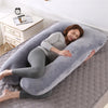 A woman lies comfortably on a gray U-shaped maternity body pillow on a floor.