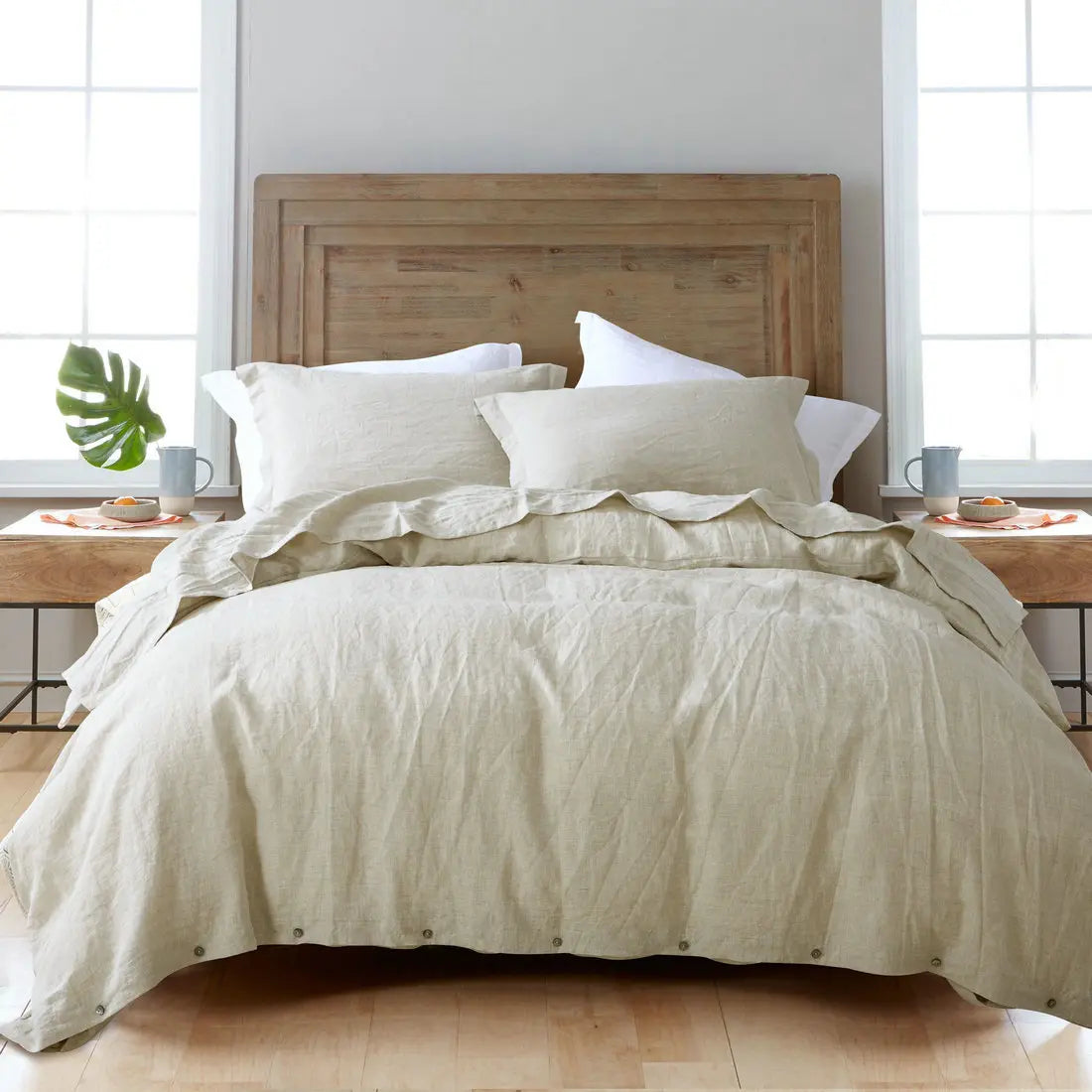 A bed dressed with a beige luxury French linen duvet cover and white pillows against a wooden headboard.