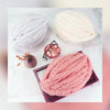 A pile of pink hand-knitted yarn is displayed on a white marble surface with small accessories.