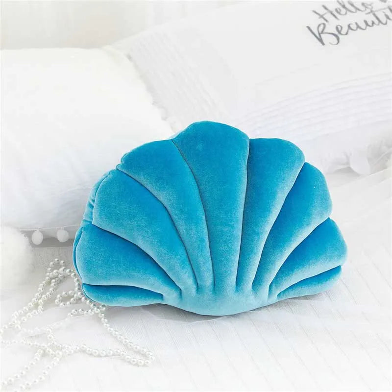 A teal velvet stuffed sofa cushion shaped like a decorative seashell resting on white fabric.